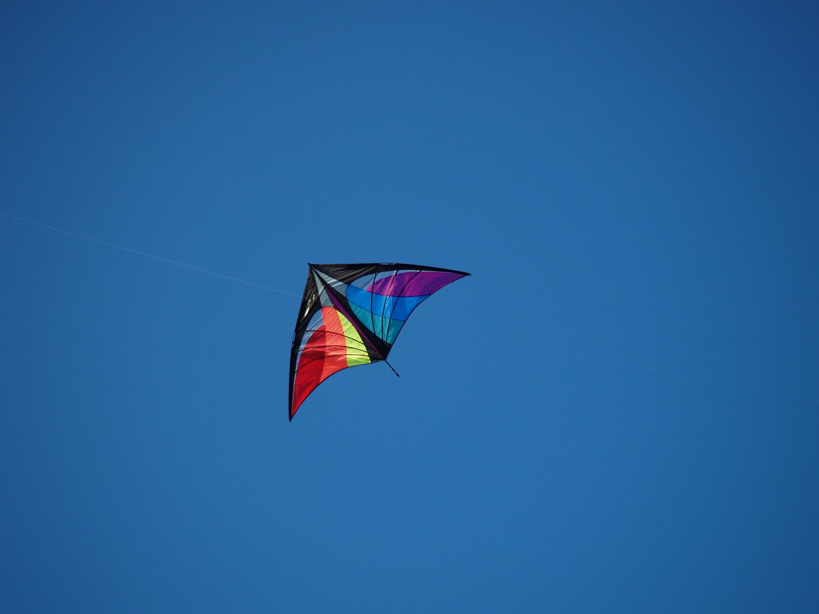 A triangular rainbow kite against a deep blue sky.