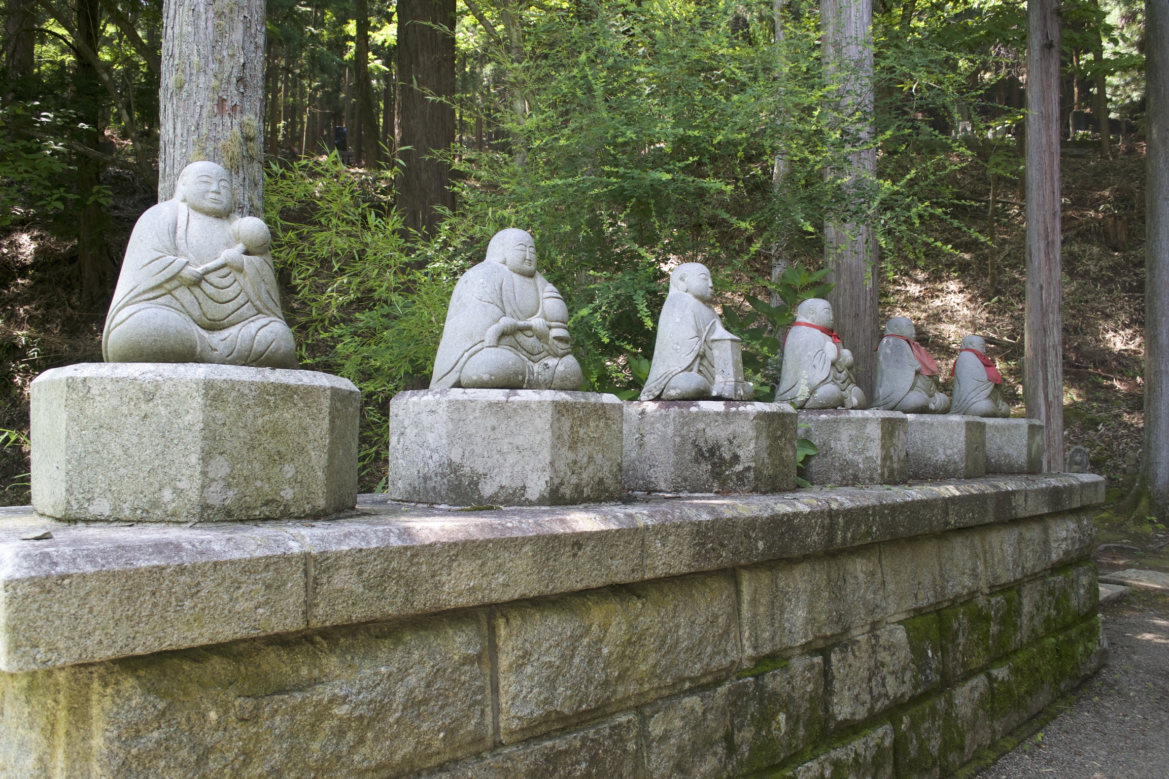 Six stone buddhas sit cross-legged, some with red cloth bibs.