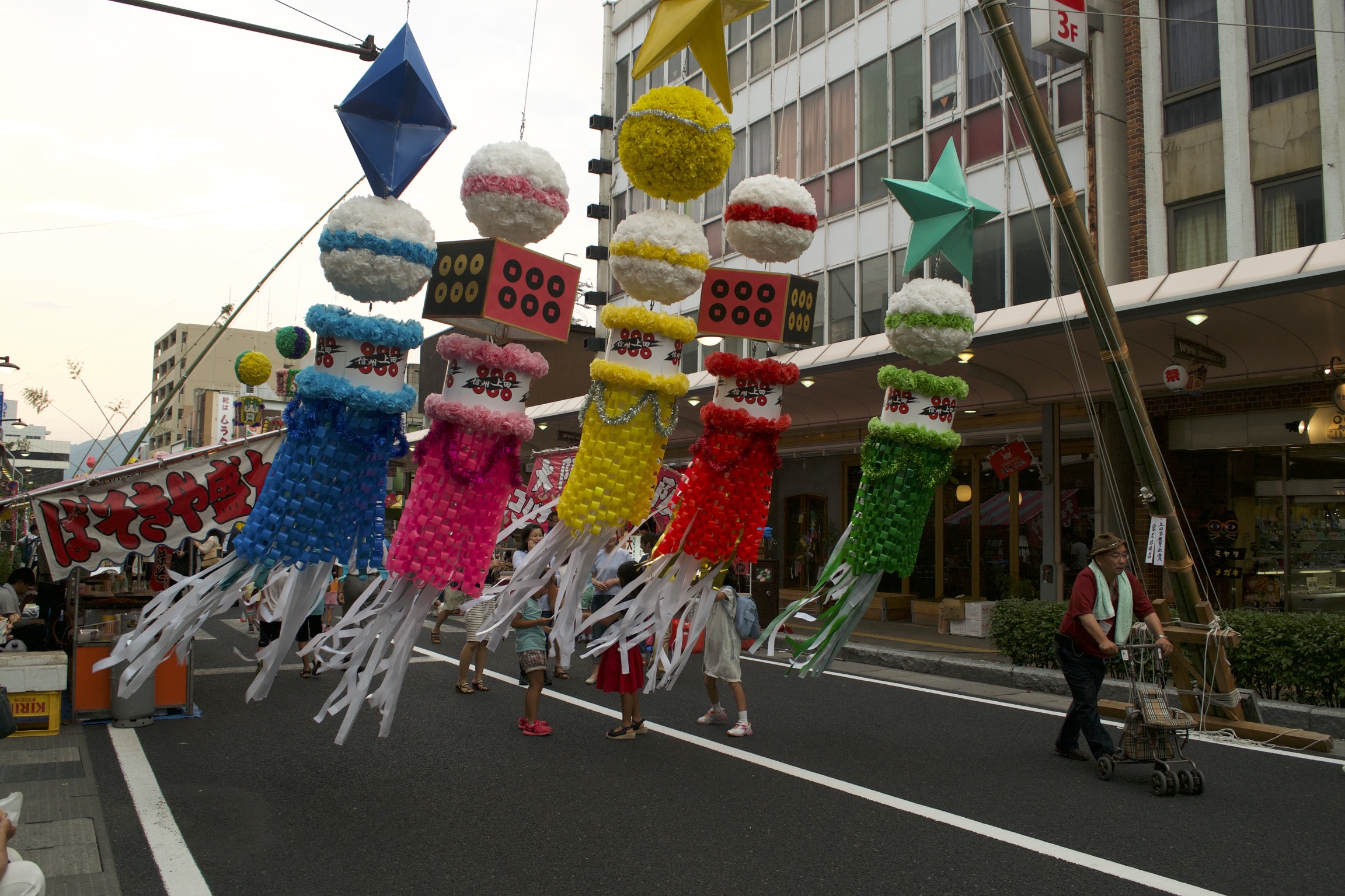 Five large, brightly-colored piñata-like objects hang in the middle of a street.