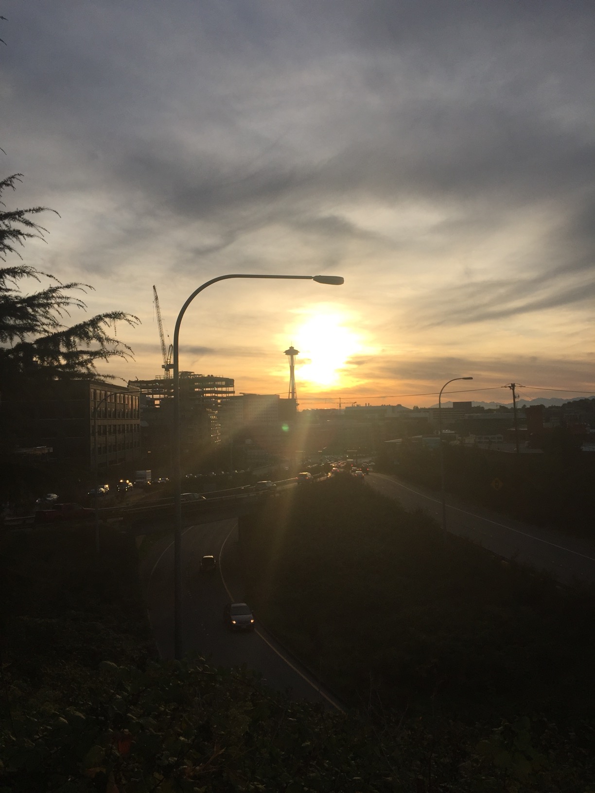The sun sets below a street lap and behind the silhouetted Space Needle.