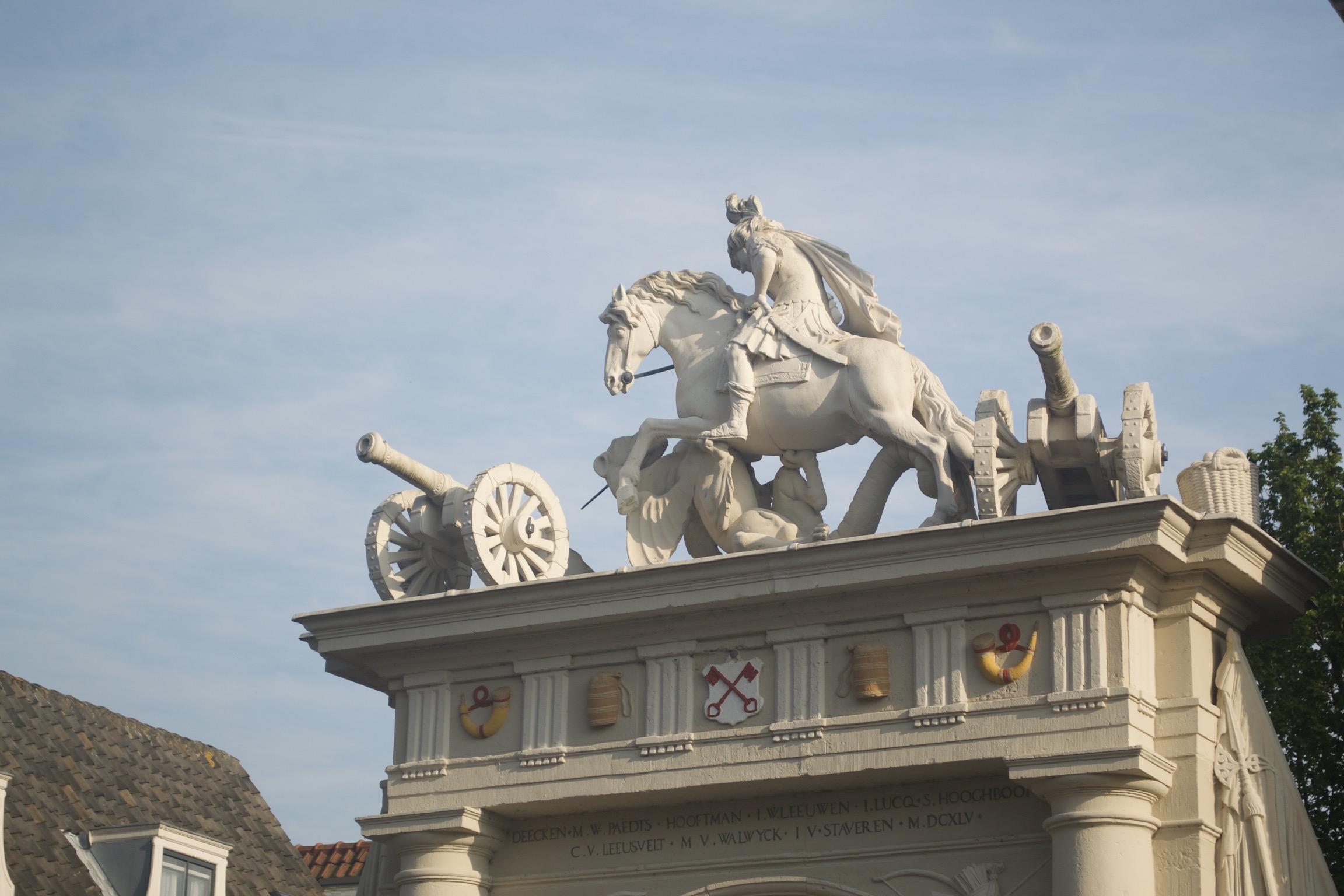 Statues of two cannons and a horse and rider fighting a griffin on top of an archway.