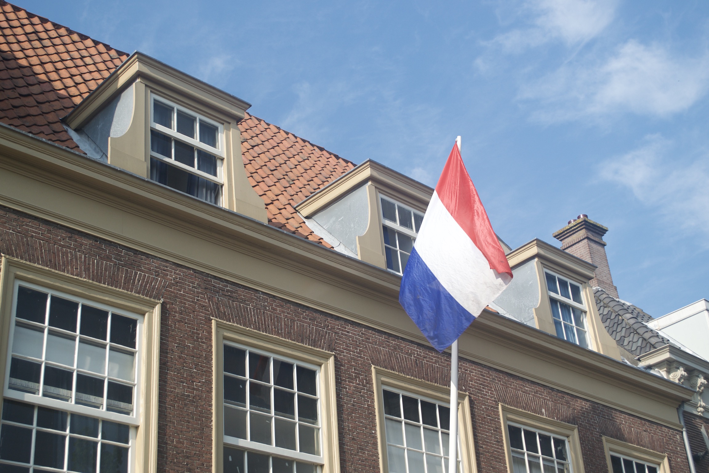 A flag of the Netherlands flys on a pole from a house.
