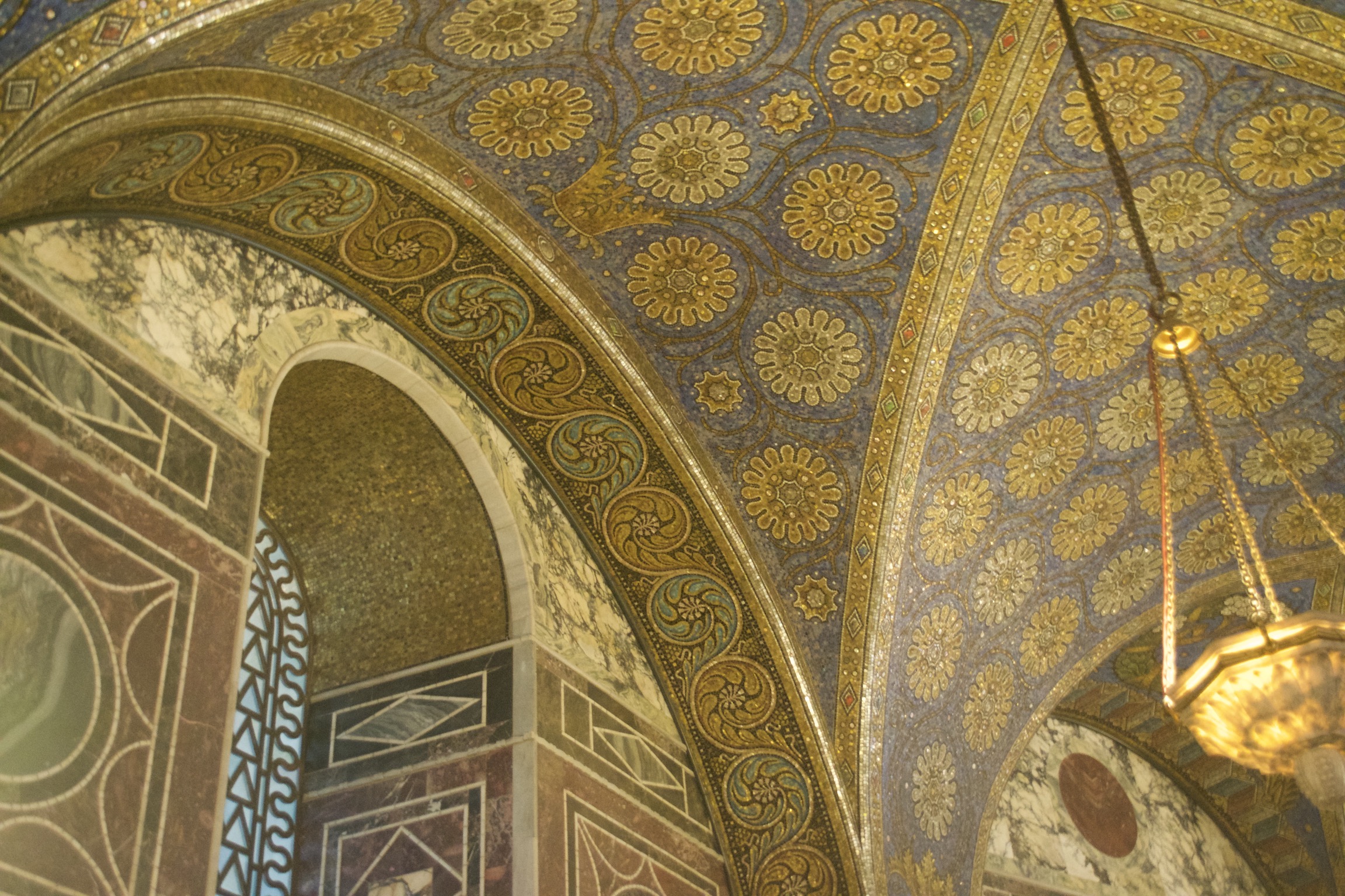 Marble and tile mosaics cover a ceiling and window arch in geometric and flowered designs.