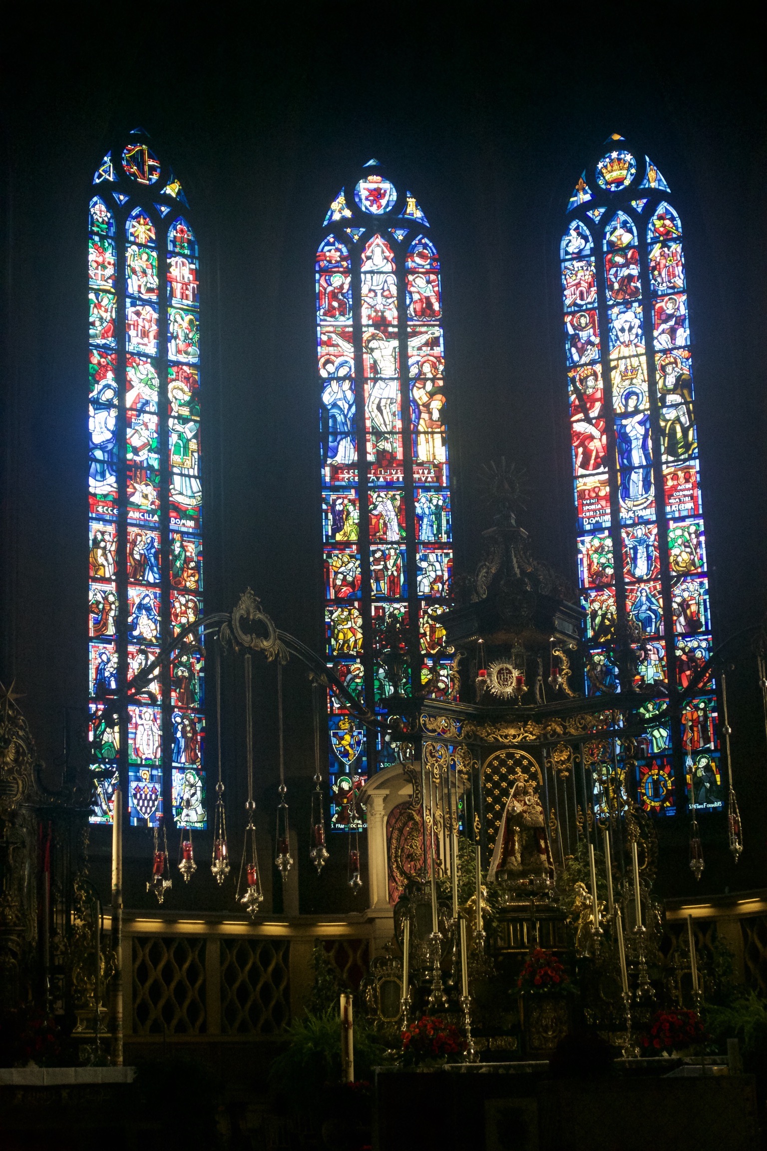 An ornate Catholic altar back lit by soaring stained glass windows.