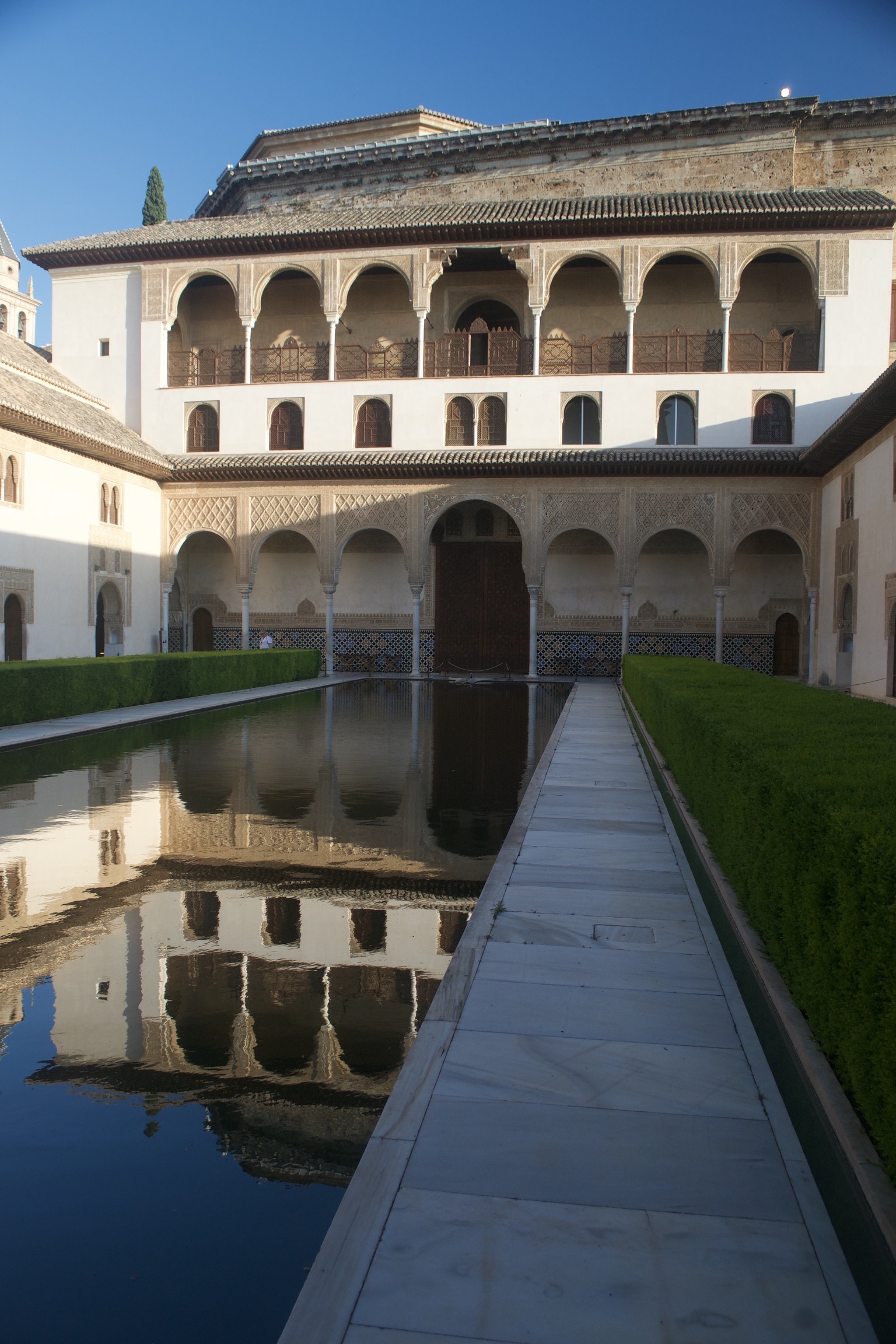A still reflecting pool mirrors a surrounding two-storied building.