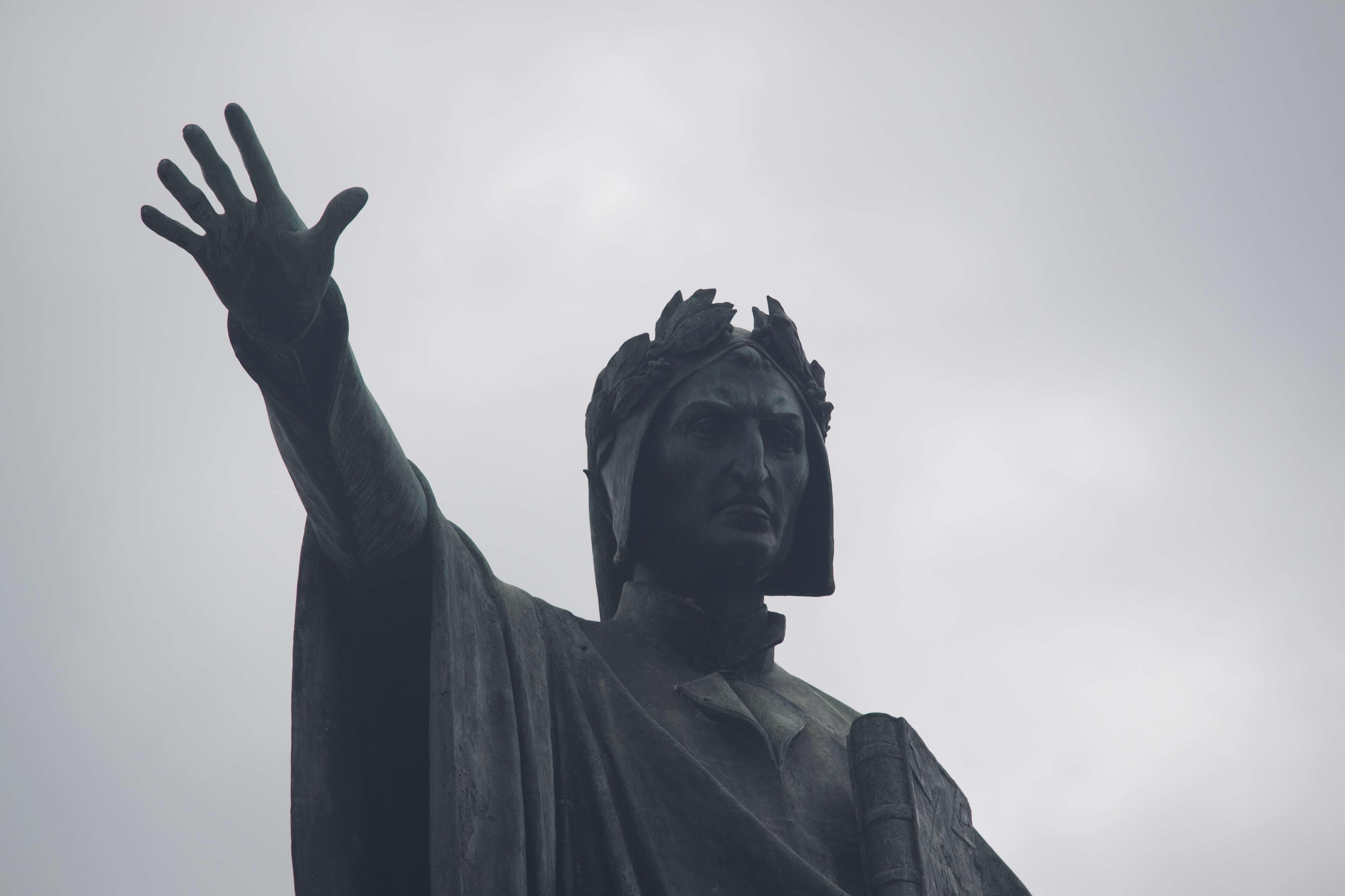 A statue of a serious man with a laurel crown extending his right hand, fingers spread.