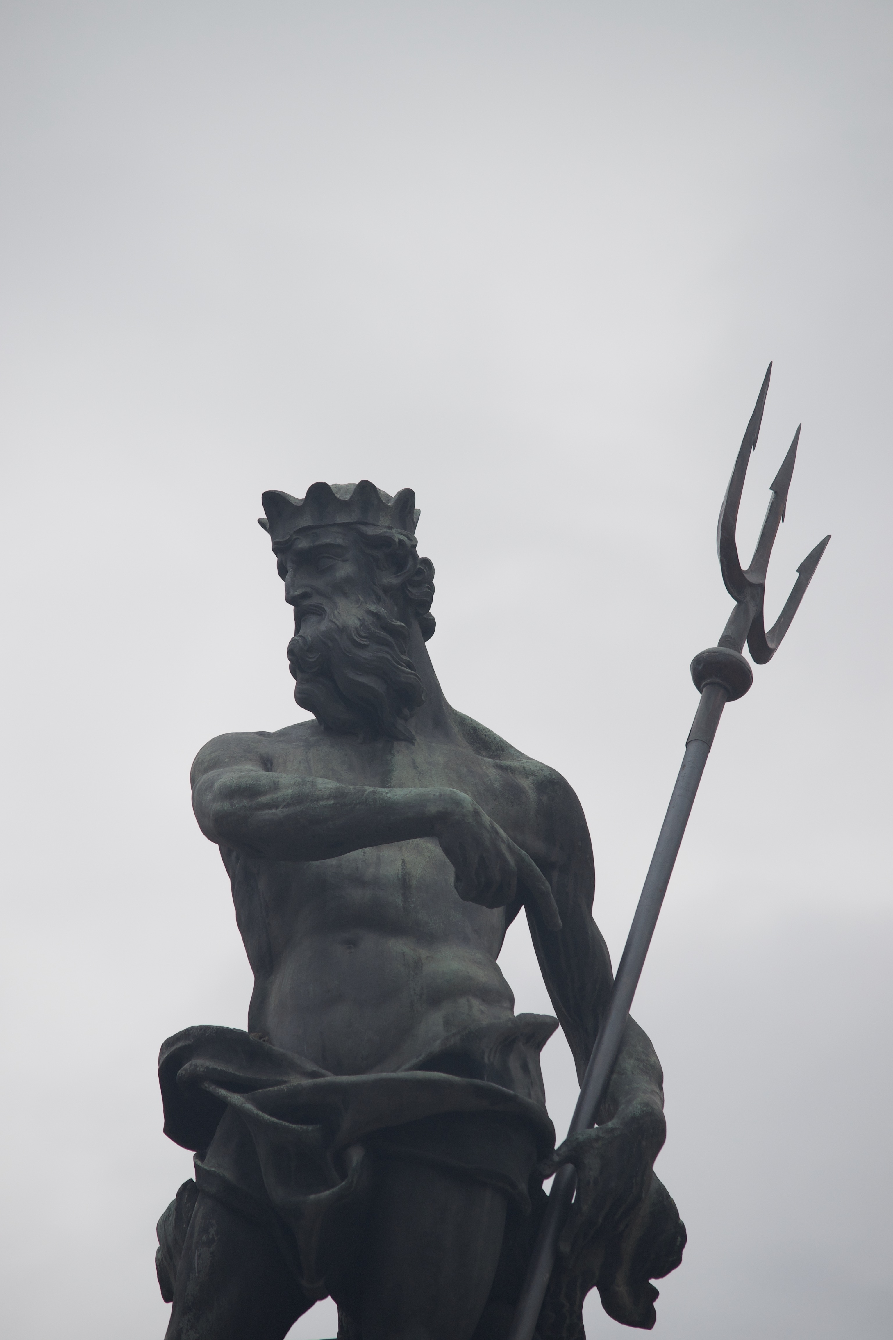 A shirtless, crowned, metal figure points with his right hand to the trident held by his left.